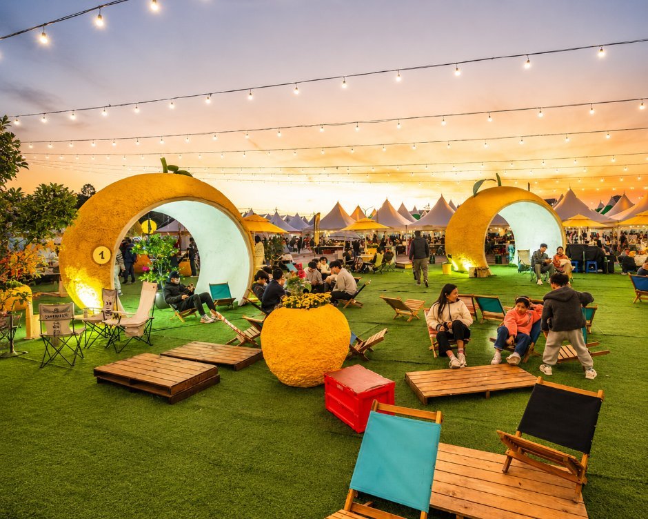 Yuja-themed lounge area with round yellow arches, deck chairs and wooden platforms at dusk at the Goheung Yuja Festival